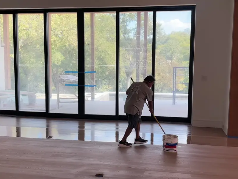Crew member applying a finish coat to a sanded hardwood floor